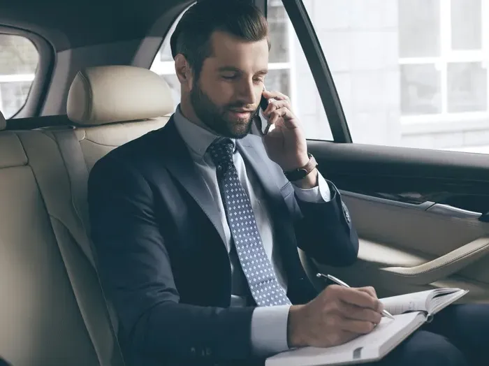 Business professional in a suit riding in a car, on the phone and writing plans in a notebook during transit
